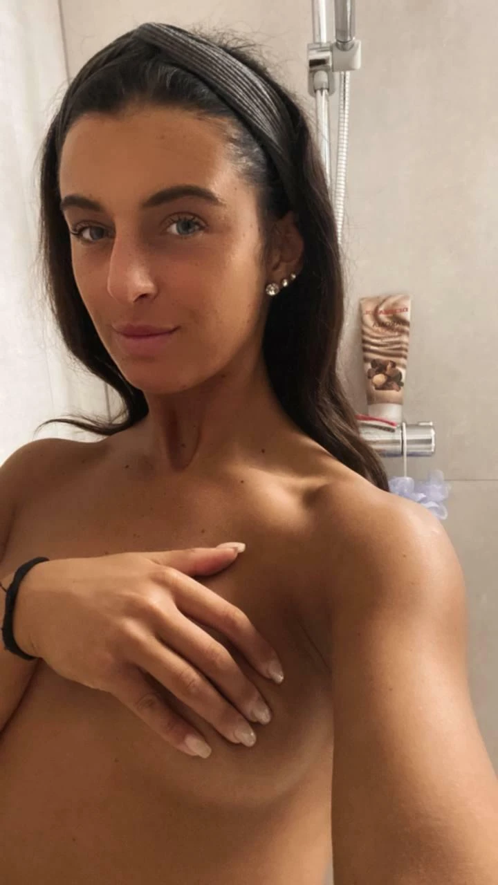 Petite woman standing nude in a spacious shower, smiling invitingly