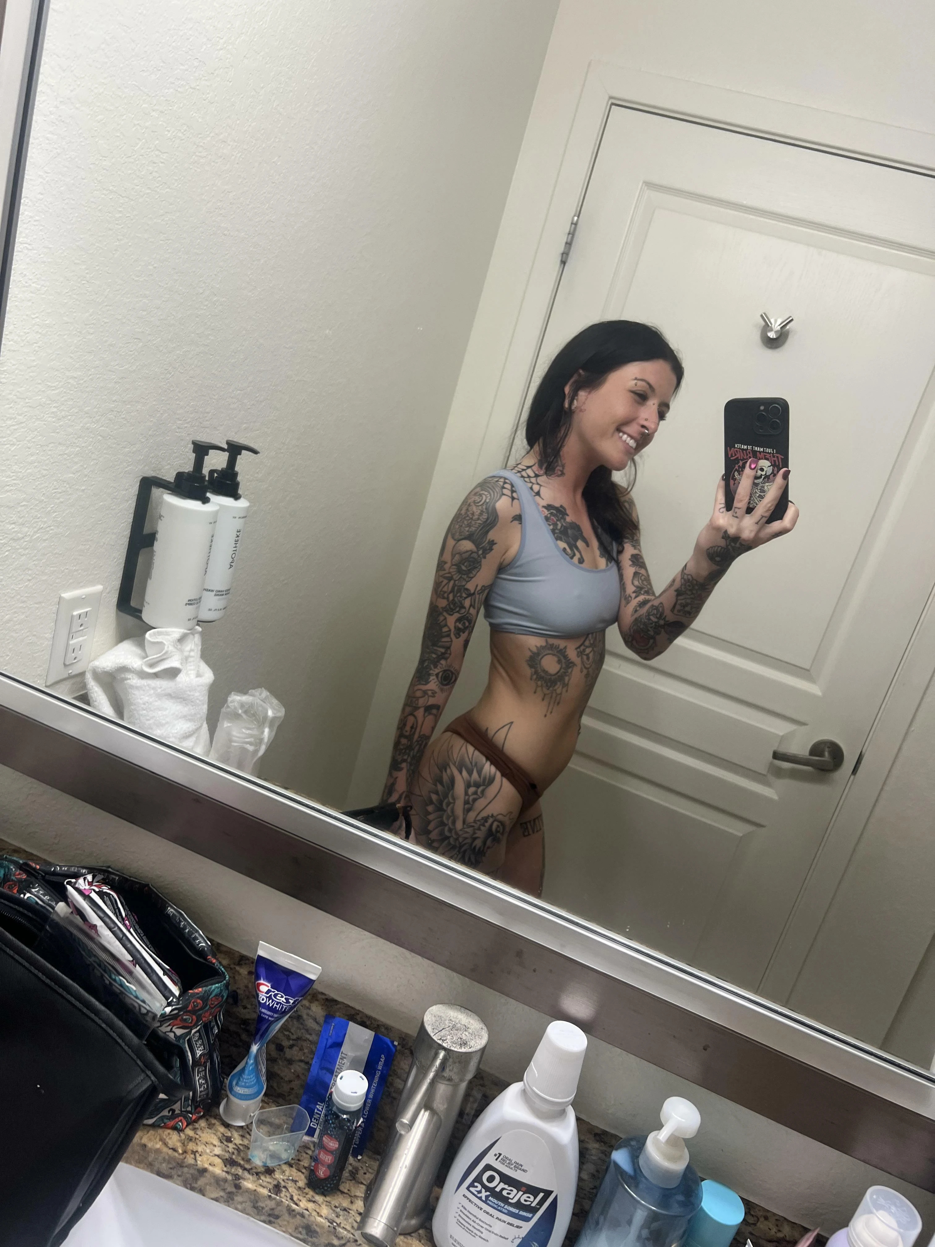 Cute young woman smiling shyly while stripping clothes off in bedroom